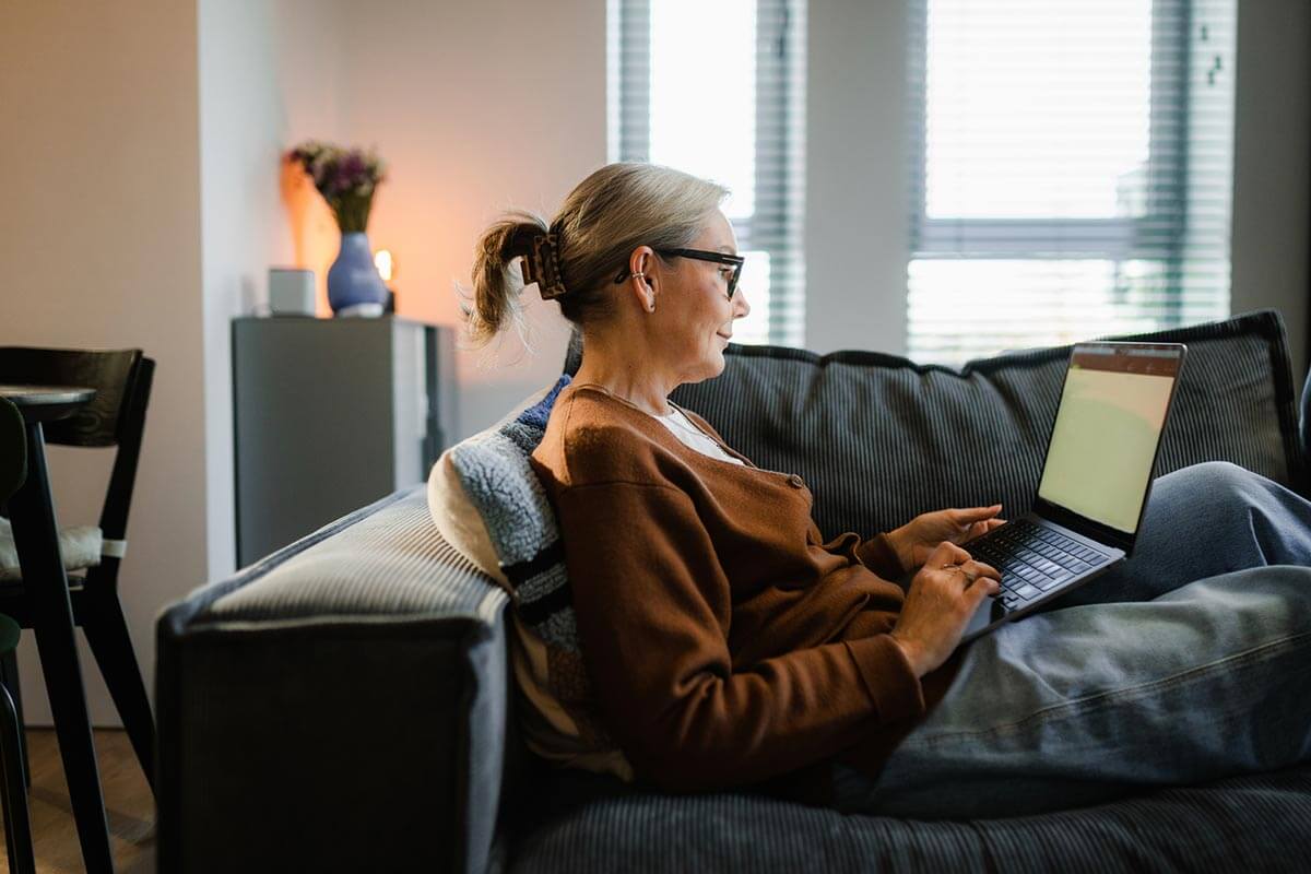 Woman on a couch typing on a laptop.